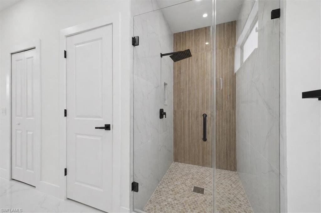 Walk-in shower featuring a rain shower head, wood-look accent wall, and mosaic tile flooring