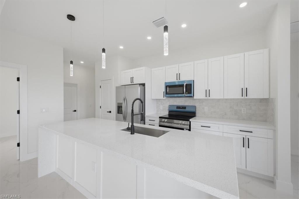 Modern kitchen featuring an expansive island with a built-in sink, white cabinetry, a light-toned tile backsplash, and stainless steel appliances