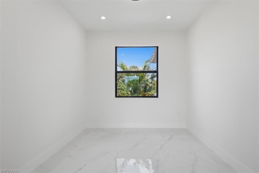 Bright interior space featuring a single window with black trim, white walls, white baseboards, and polished tile flooring