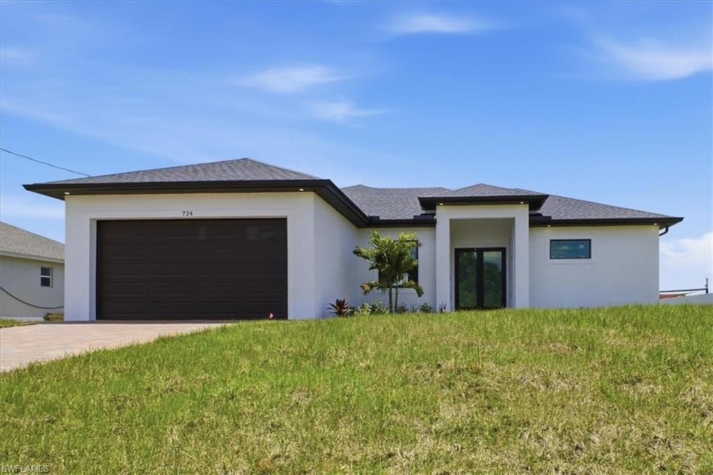 Contemporary architecture featuring a white stucco exterior, dark shingle roof, dark garage door, and a covered entry with double glass doors