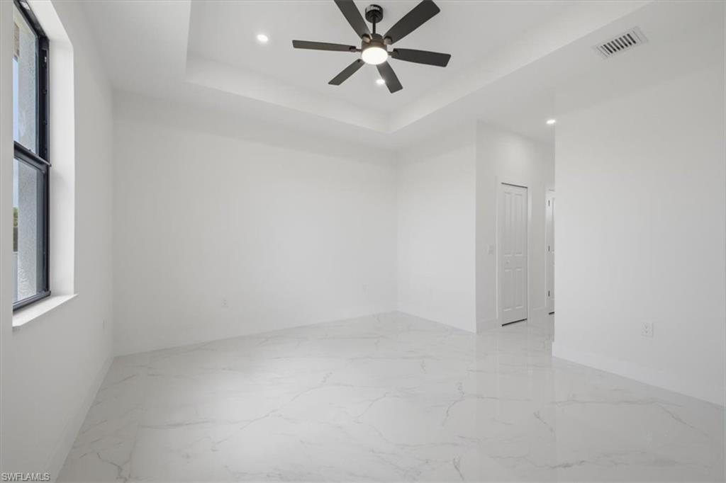 Spacious room featuring white tile flooring, tray ceiling, recessed lighting, and a ceiling fan with integrated light