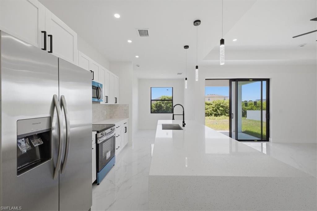Modern kitchen featuring a large white quartz island with a black faucet, stainless steel appliances, white cabinetry with black hardware, and large format tile flooring