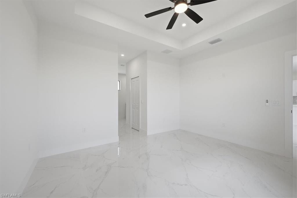 Spacious room featuring large format tile flooring, a tray ceiling with a ceiling fan, recessed lighting, and a paneled interior door