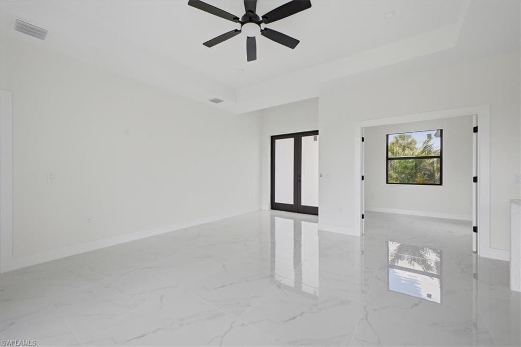 Spacious interior featuring large format tile flooring, a tray ceiling, and a modern ceiling fan