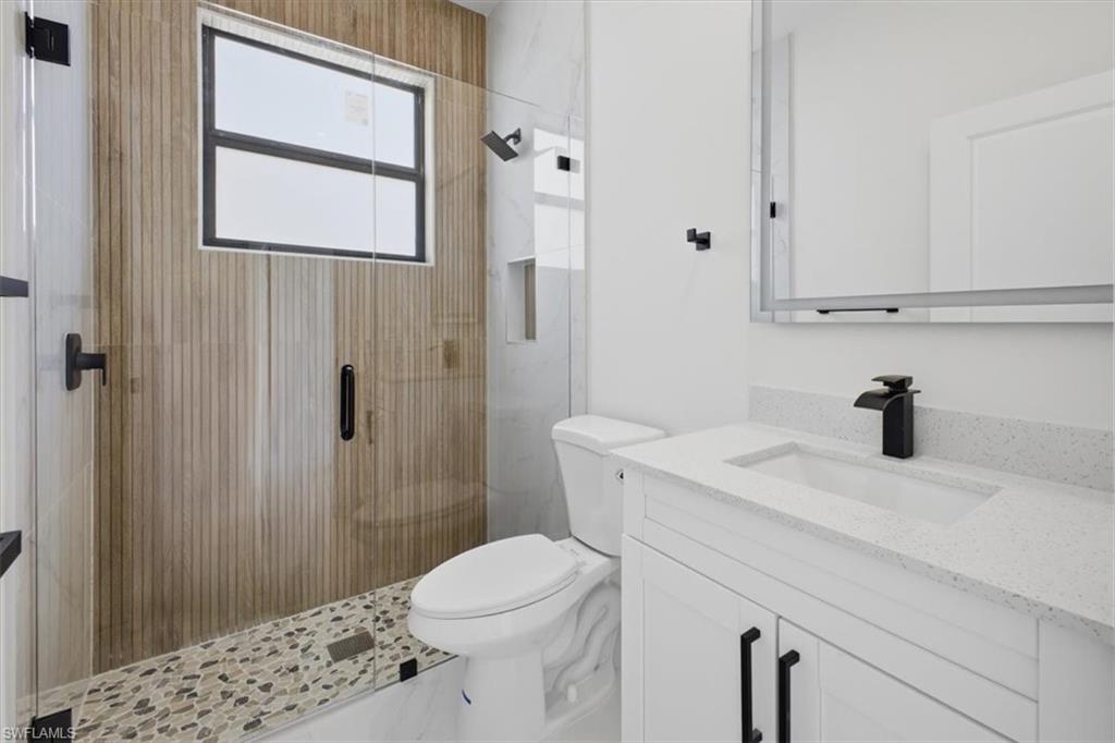 Contemporary bathroom featuring a glass-enclosed shower with wood-finish vertical paneling, a pebble-tiled shower floor, and a black-framed window