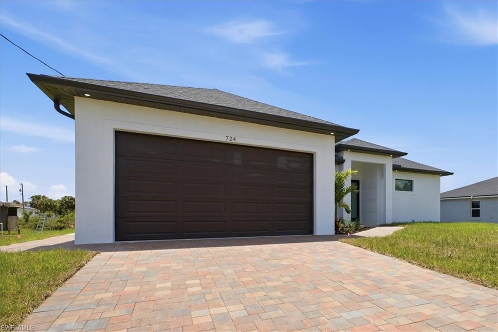Contemporary-style residence with a dark brown garage door, white stucco exterior, and a multi-toned paver driveway