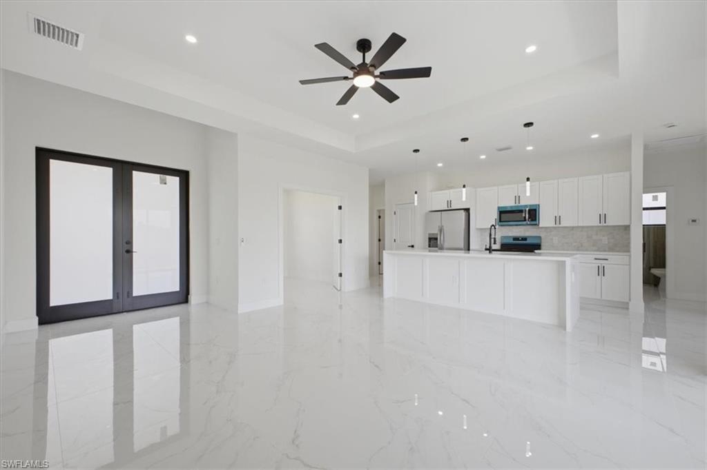 Bright open concept space featuring large-format tile flooring, a modern kitchen island, white cabinetry, and stainless steel appliances