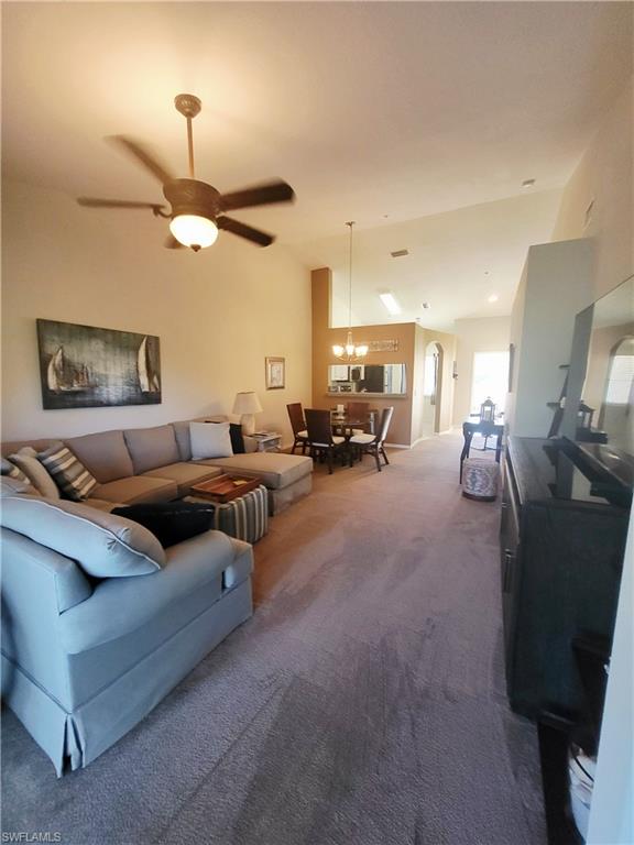 Carpeted living room with ceiling fan, arched walkways, and lofted ceiling