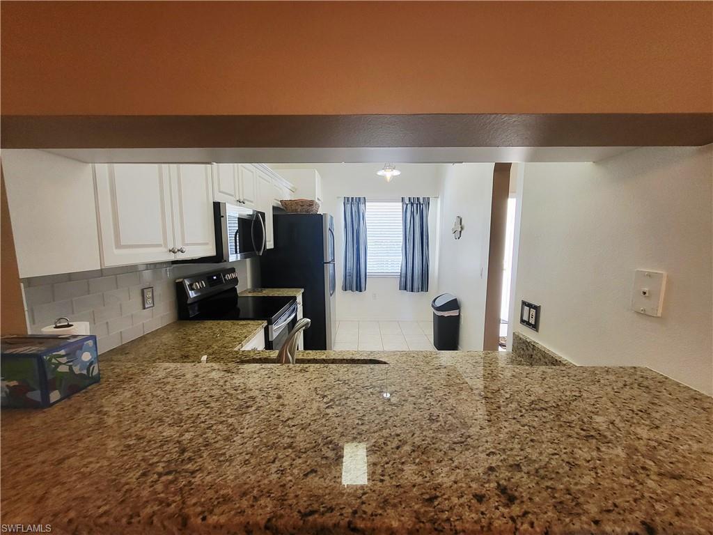 Kitchen featuring white cabinetry, light stone countertops, electric range, and stainless steel microwave