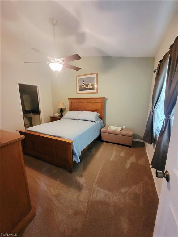 Carpeted bedroom with ceiling fan, vaulted ceiling, and ensuite bath