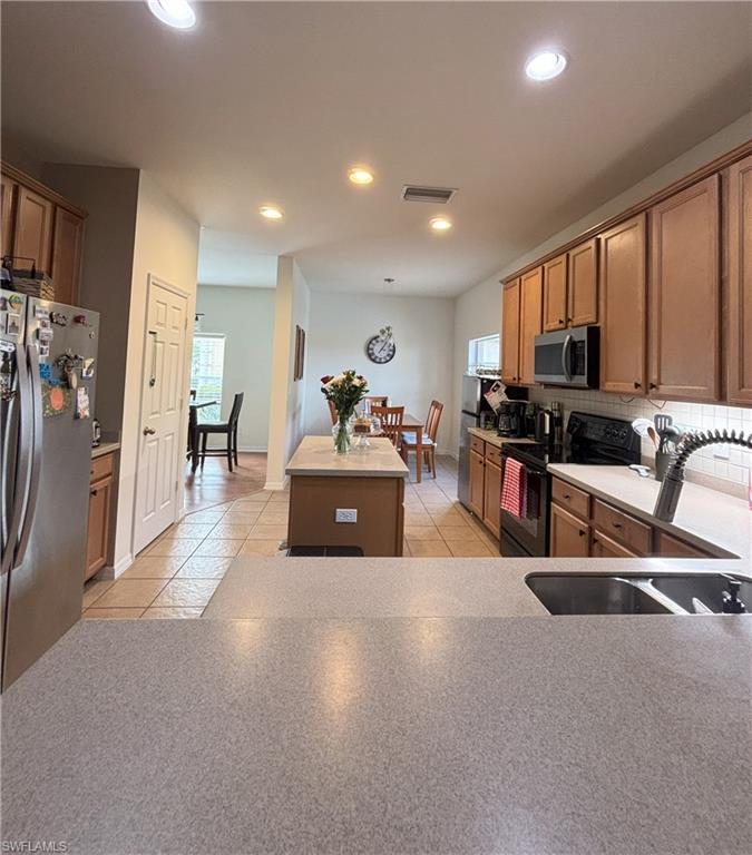Kitchen with appliances with stainless steel finishes, a kitchen island, brown cabinets, tasteful backsplash, and recessed lighting