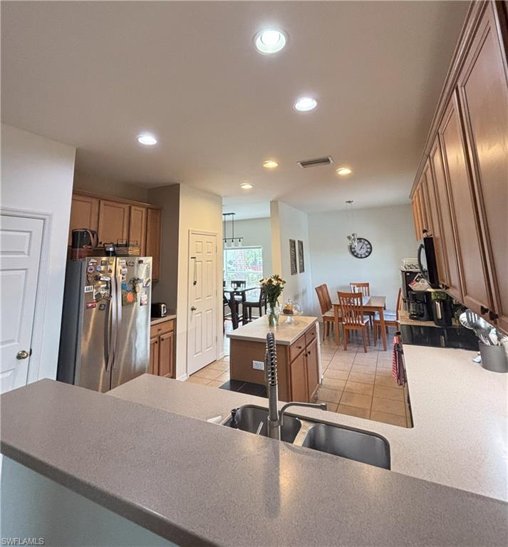Kitchen featuring freestanding refrigerator, brown cabinets, a center island, recessed lighting, and hanging light fixtures