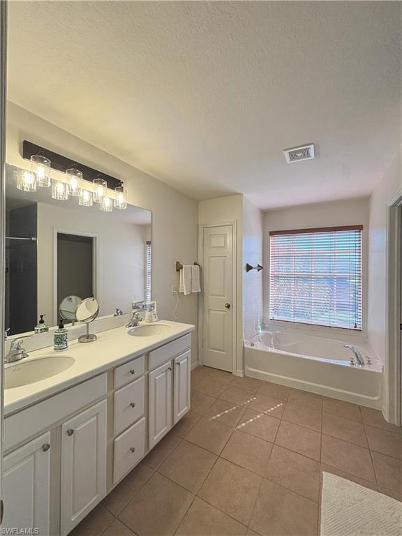 Bathroom with a textured ceiling, a garden tub, double vanity, and light tile patterned floors