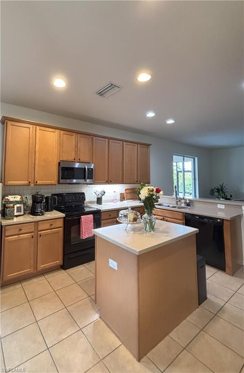 Kitchen with a kitchen island, black appliances, a peninsula, light tile patterned floors, and brown cabinets