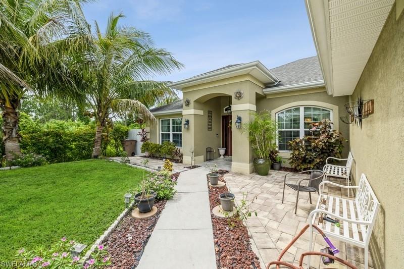Doorway to property featuring stucco siding, a yard, and roof with shingles