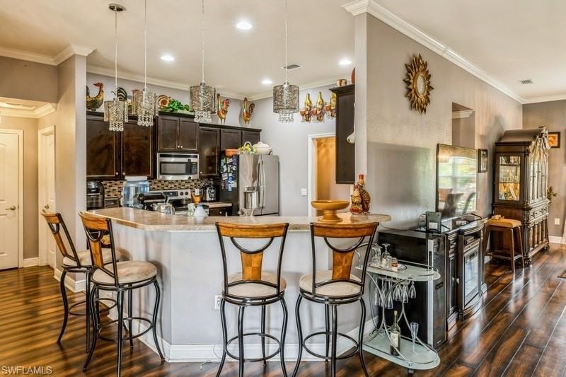 Kitchen featuring hanging light fixtures, dark brown cabinetry, appliances with stainless steel finishes, decorative backsplash, and a kitchen breakfast bar