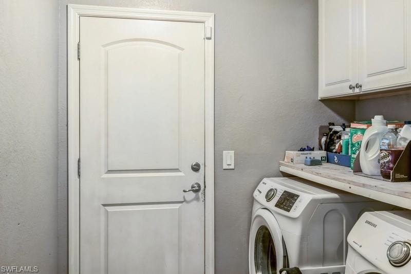 Laundry room featuring a textured wall, cabinet space, and washer and dryer