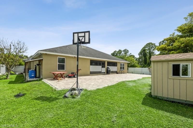 Rear view of property featuring a patio area, a storage unit, a fenced backyard, a sunroom, and board and batten siding