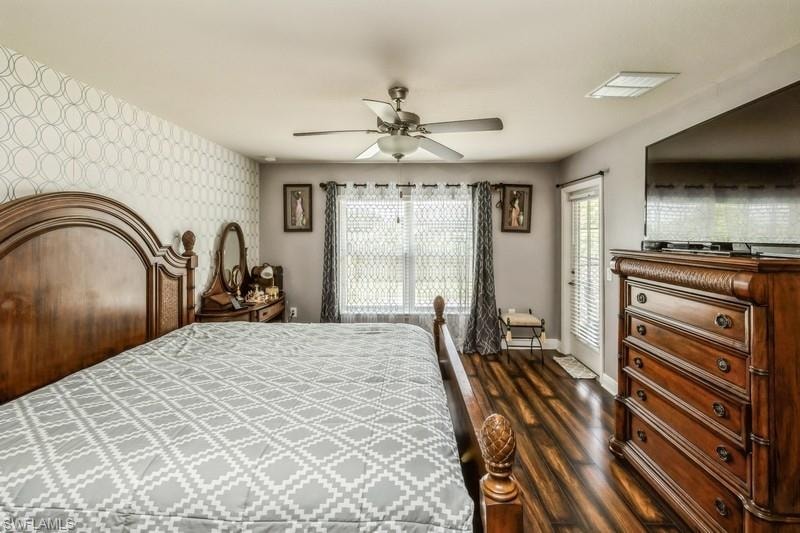 Bedroom featuring wallpapered walls, an accent wall, dark wood-type flooring, and a ceiling fan