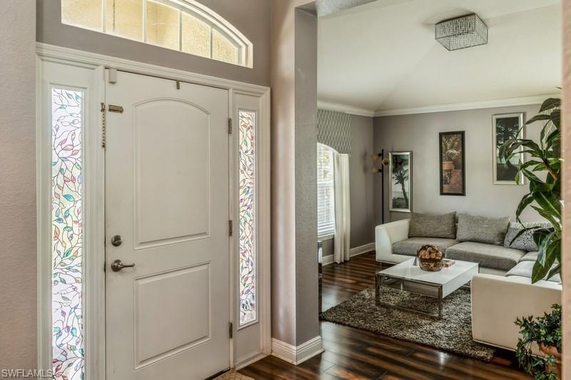 Entryway with dark wood-type flooring, crown molding, and vaulted ceiling