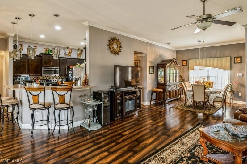 Living room with a ceiling fan, ornamental molding, and dark wood-style floors