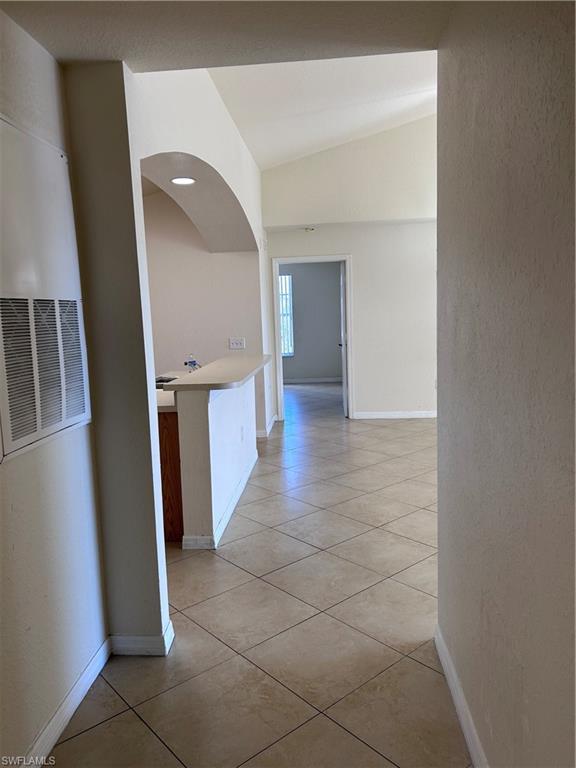 Hallway with light tile patterned floors, vaulted ceiling, a heating unit, and a textured wall