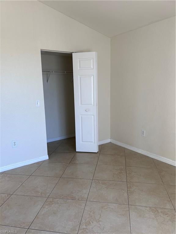 Unfurnished bedroom with vaulted ceiling, a closet, and light tile patterned floors