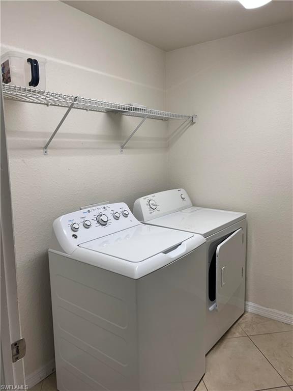 Laundry area with light tile patterned floors, separate washer and dryer, and a textured wall
