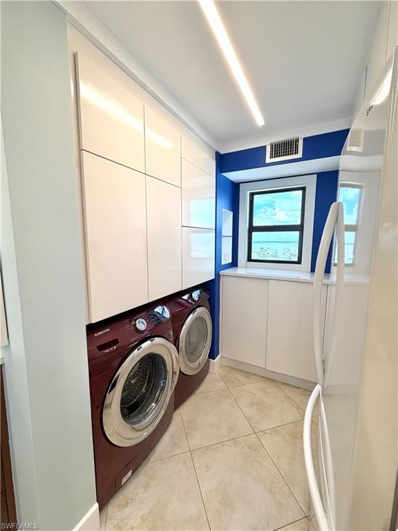 Modern laundry room featuring front-load washer/ dryer in rich burgundy finish, tile flooring, recessed ceiling lighting, white cabinetry with upper storage, and a blue accent wall with windows for natural light