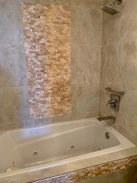Recessed ceiling lighting with a crystal chandelier, tiled bathtub surround with an integrated shower, wall-mounted floating shelf, vanity with an integrated sink, and a wood-framed mirror