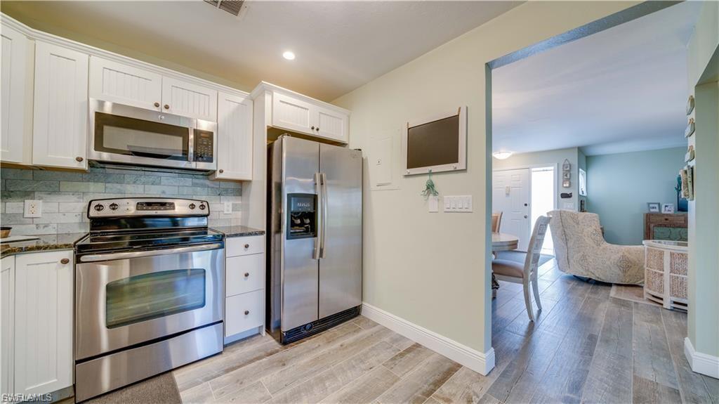 Kitchen with stainless steel appliances, white cabinets, dark stone counters, and decorative backsplash