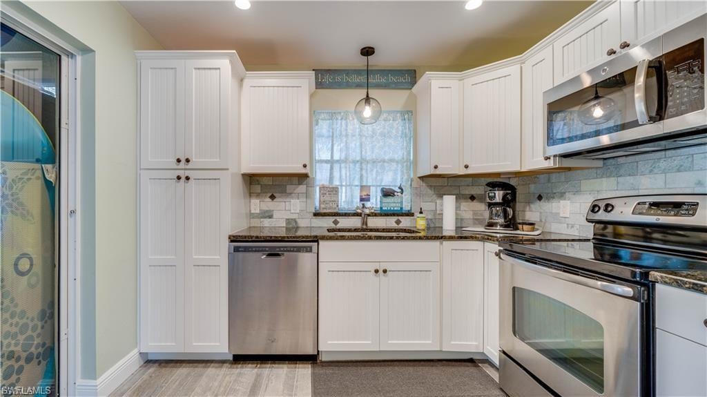 Kitchen featuring stainless steel appliances, tasteful backsplash, white cabinets, and hanging light fixtures