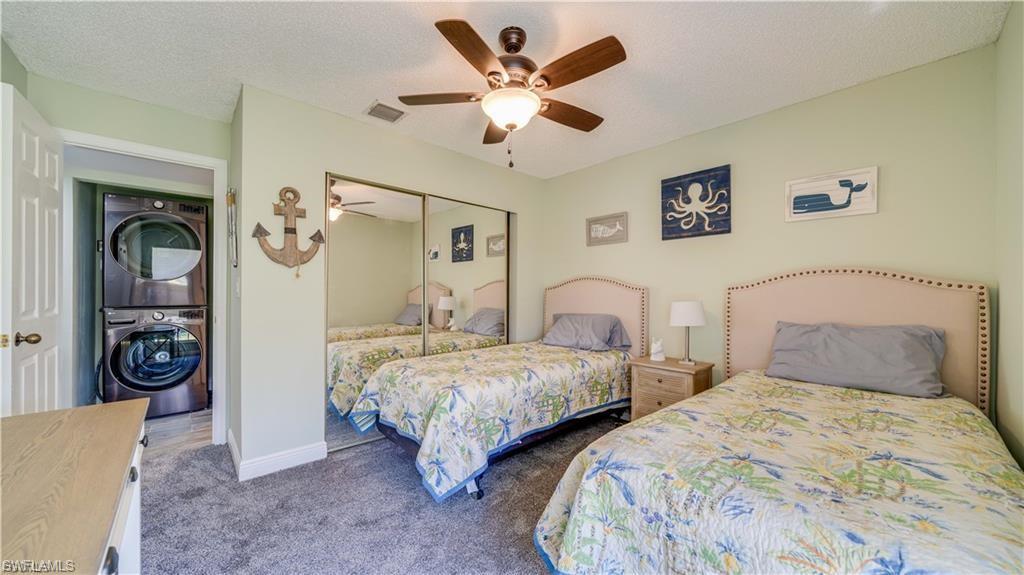 Bedroom with stacked washer and dryer, dark carpet, a ceiling fan, a closet, and a textured ceiling