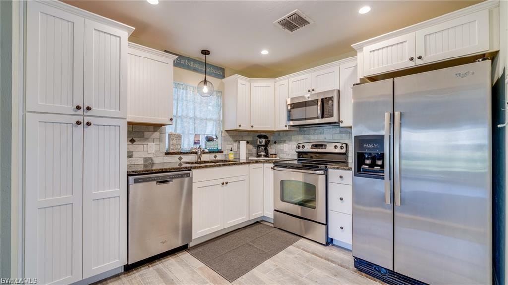 Kitchen with stainless steel appliances, decorative light fixtures, white cabinetry, backsplash, and wood tiled floors