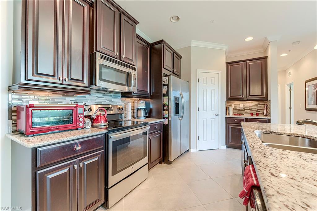 Kitchen with appliances with stainless steel finishes, ornamental molding, decorative backsplash, dark brown cabinets, and light tile patterned floors