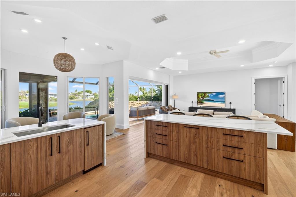 Kitchen with brown cabinets, modern cabinets, light stone countertops, open floor plan, and hanging light fixtures
