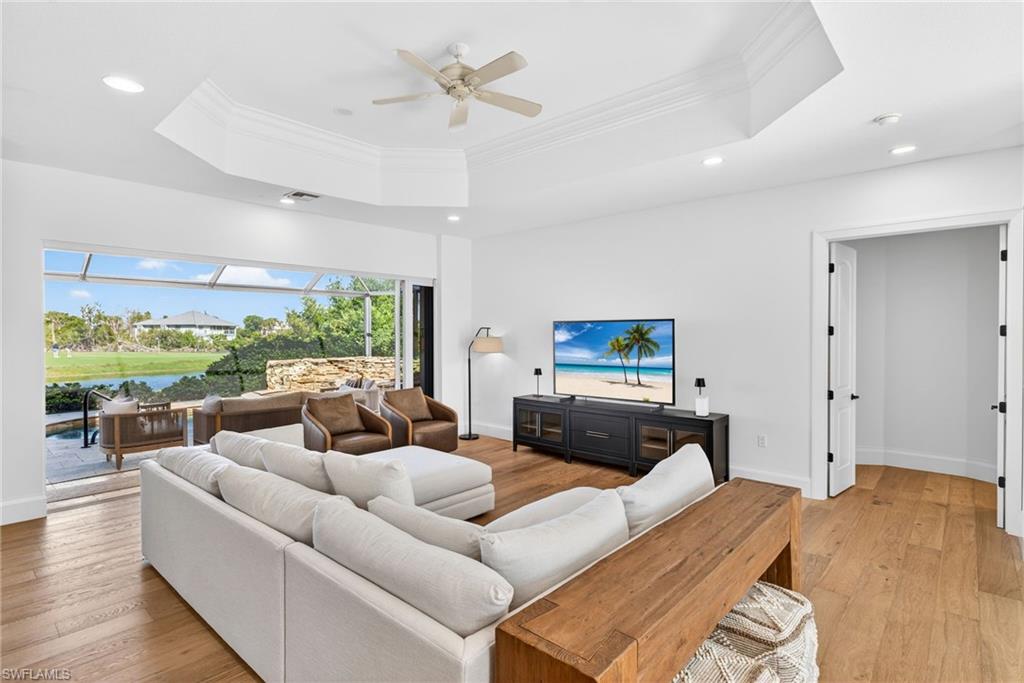 Living area with a ceiling fan, light wood finished floors, a raised ceiling, ornamental molding, and a water view
