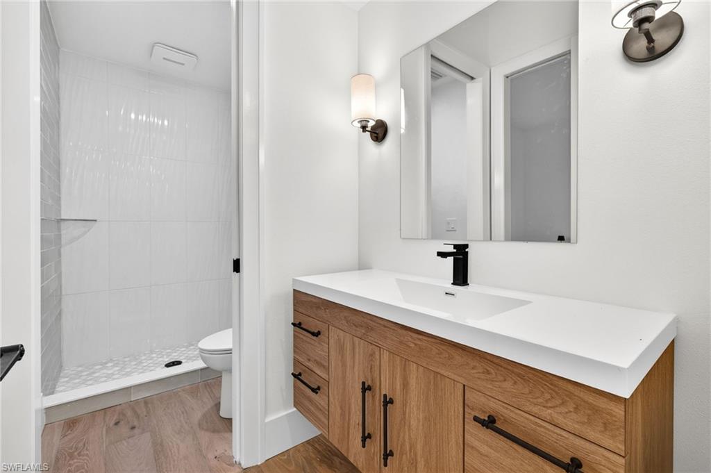 Full bath with vanity, light wood finished floors, and tiled shower