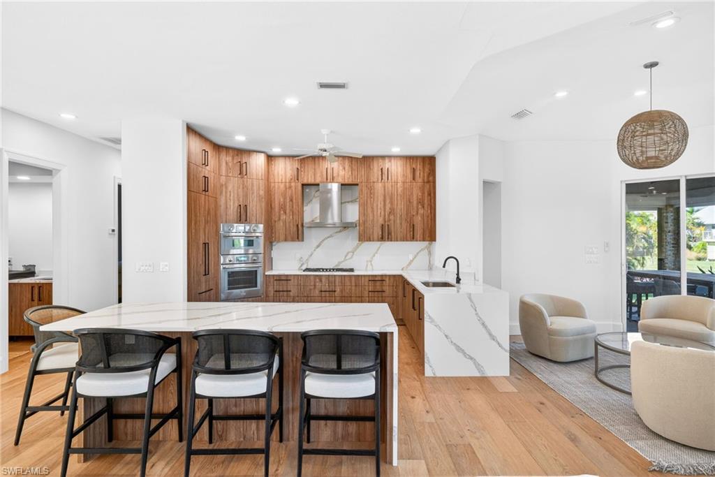 Kitchen with brown cabinets, a kitchen breakfast bar, light stone counters, modern cabinets, and recessed lighting