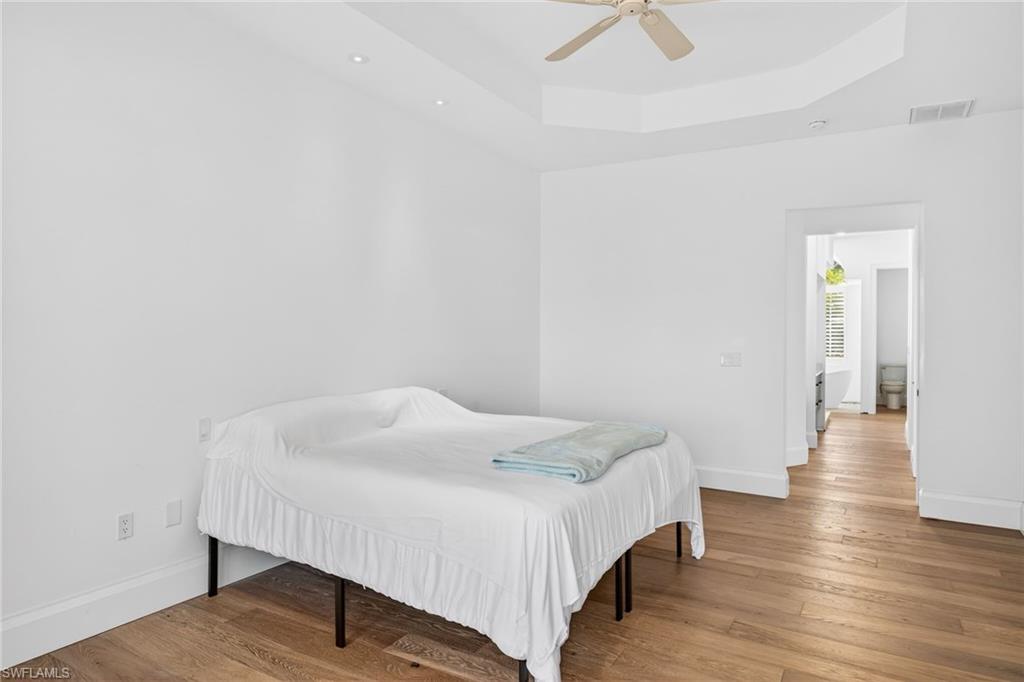 Bedroom featuring a raised ceiling, light wood-style floors, and a ceiling fan