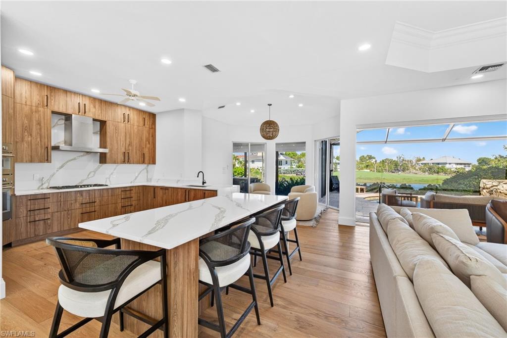 Kitchen featuring modern cabinets, open floor plan, a kitchen bar, light stone counters, and recessed lighting