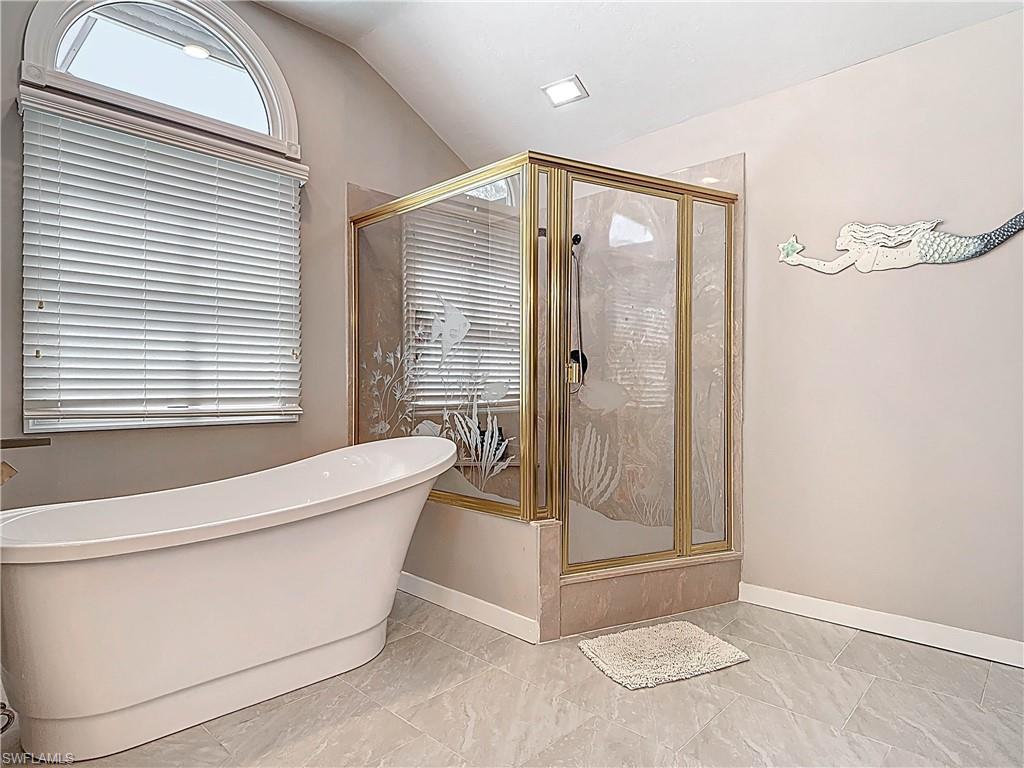 Bathroom featuring a shower stall, a freestanding tub, and vaulted ceiling