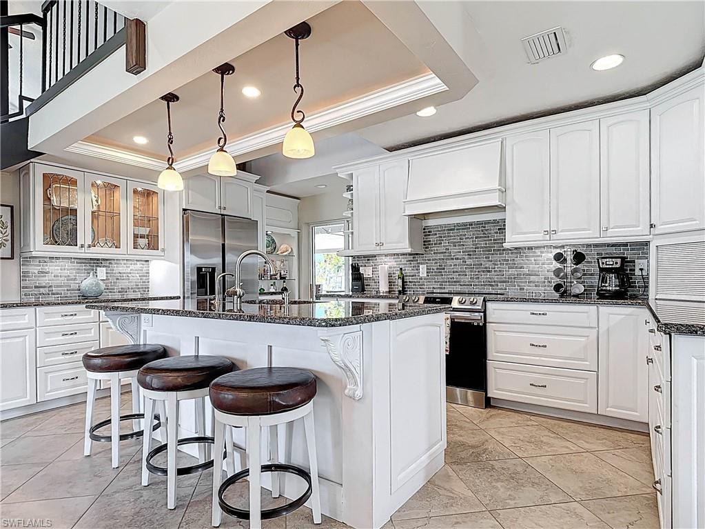 Kitchen with white cabinets, dark stone counters, a kitchen bar, an island with sink, and recessed lighting
