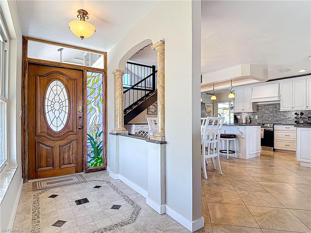 Entrance foyer with inlaid floor details, light tile patterned floors, arched walkways, ornate columns, and stairway