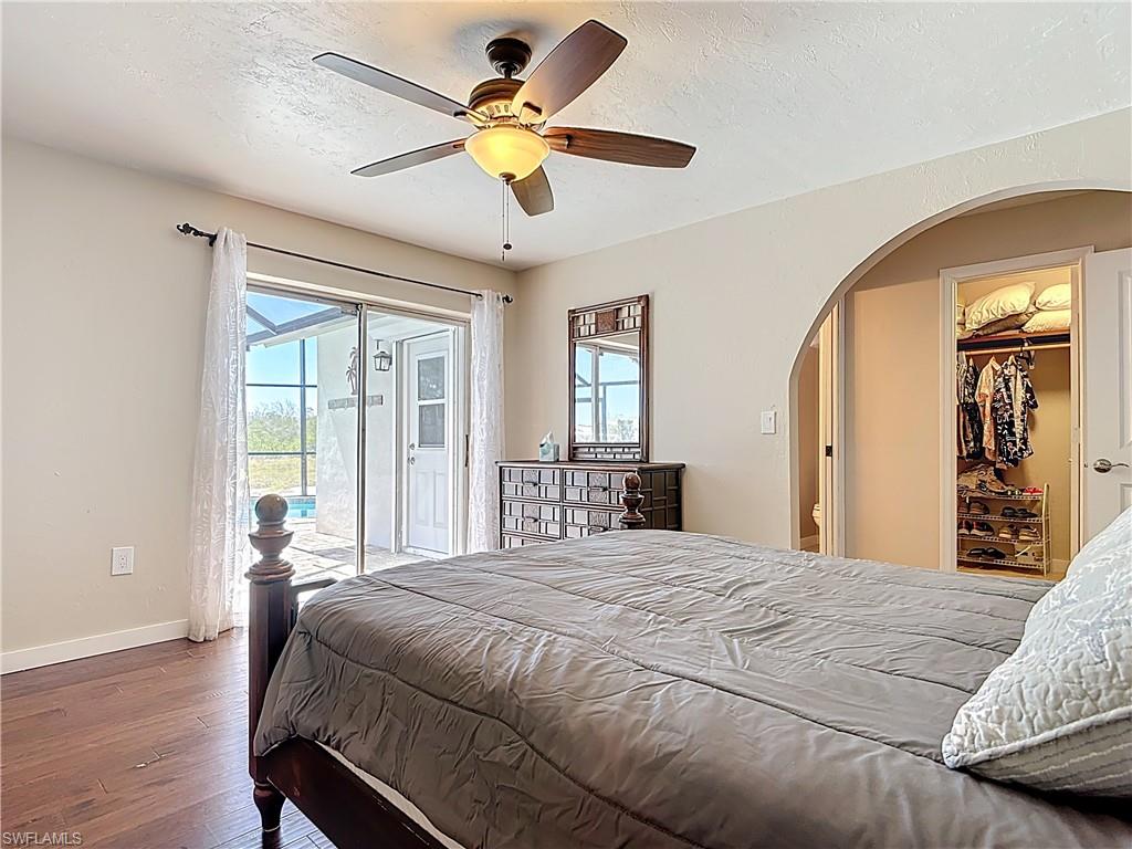 Bedroom featuring multiple windows, a textured ceiling, a walk in closet, wood-type flooring, and access to exterior