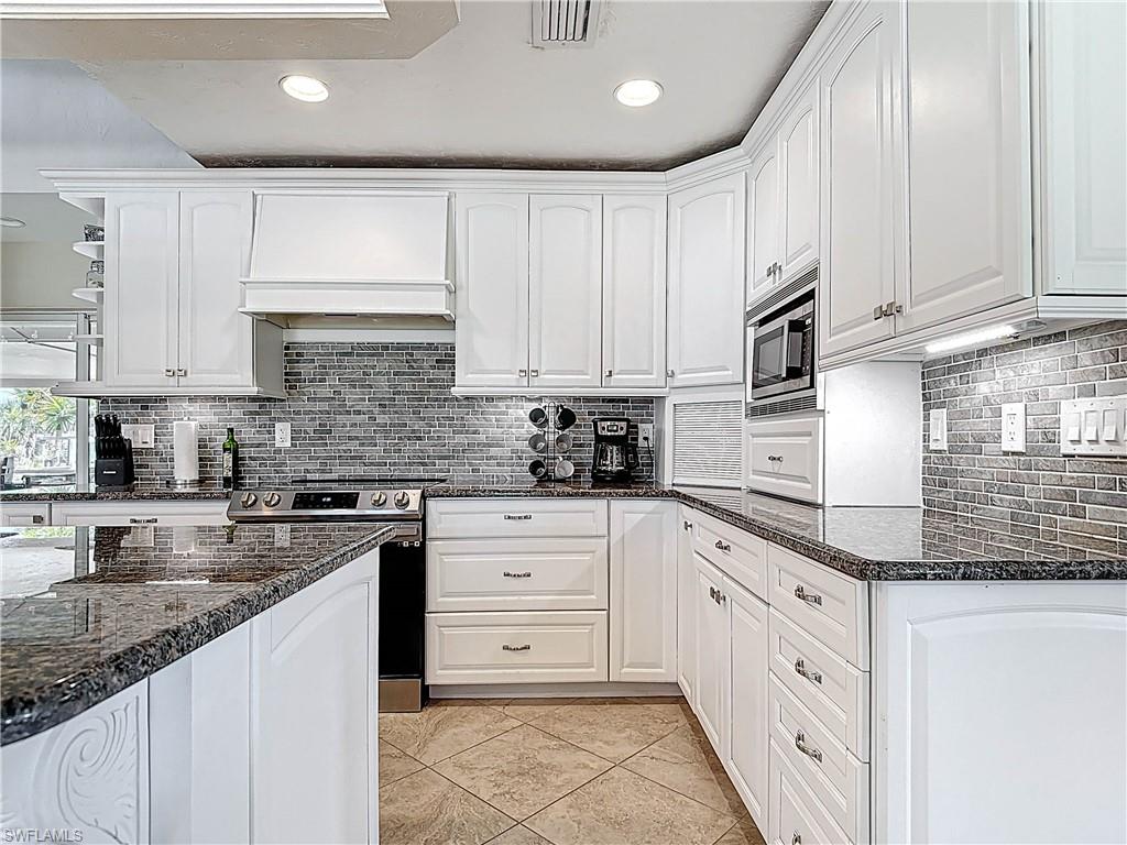 Kitchen with dark stone countertops, white cabinets, appliances with stainless steel finishes, and recessed lighting