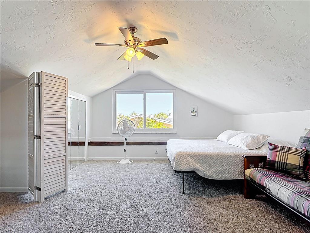 Carpeted bedroom featuring a textured ceiling, lofted ceiling, and ceiling fan