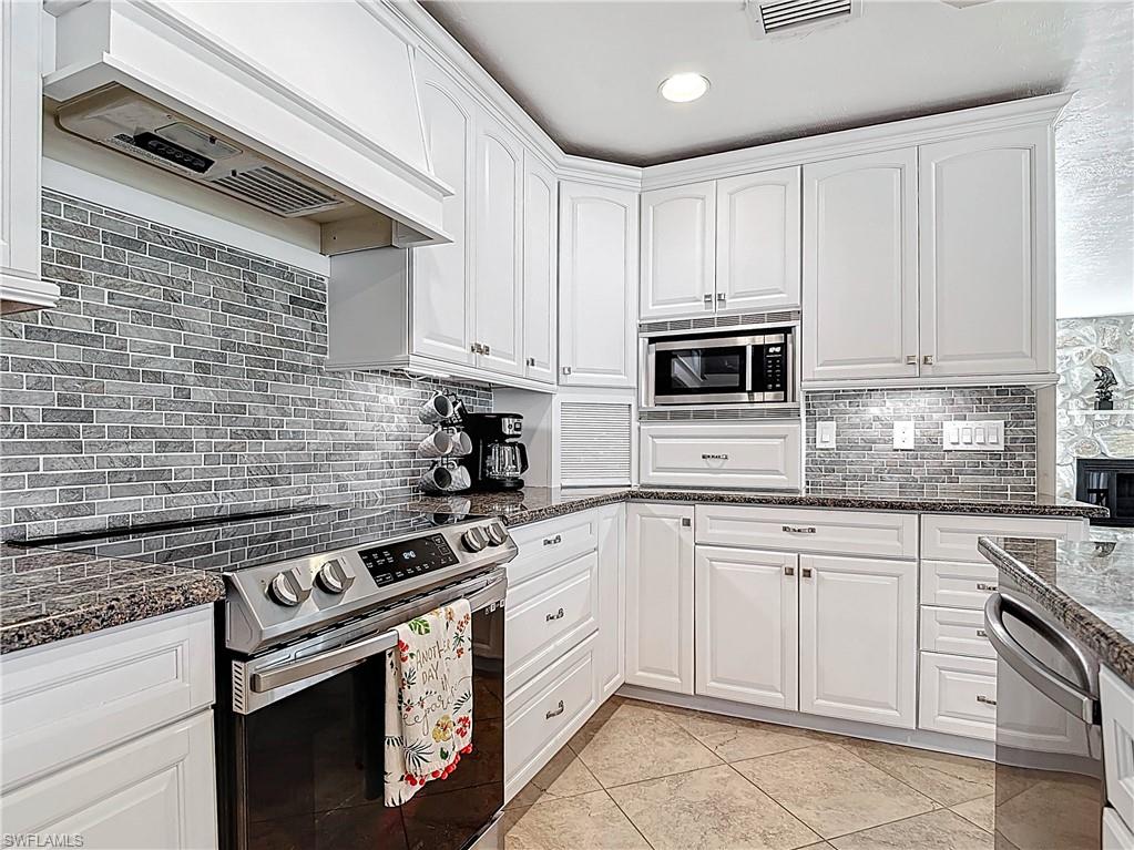Kitchen with stainless steel appliances, white cabinets, premium range hood, and recessed lighting