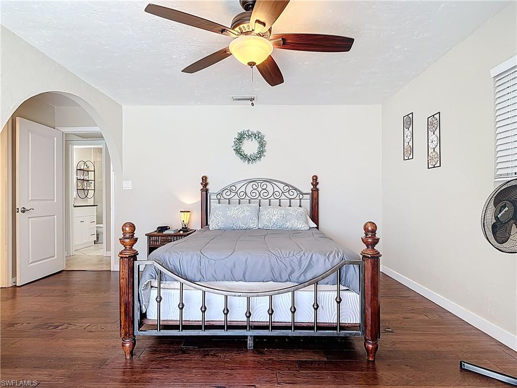 Bedroom with dark wood-type flooring, a textured ceiling, a ceiling fan, and arched walkways