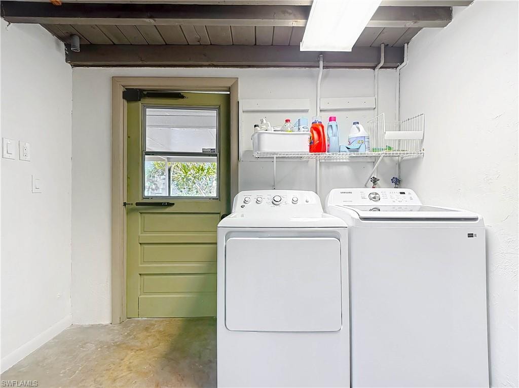Laundry room with unfinished concrete flooring, a wood ceiling with exposed beams, and washer and clothes dryer